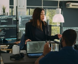 Asian database programer explaining software development with server code, using laptop to show terminal window to coder. App developer typing big data for firewall security in agency office.