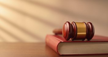 Law book and wooden judges gavel on a wooden table top in a shaft of sunlight with rayed shadow effect, conceptual image of law enforcement with copyspace
