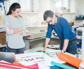 Confident young specialists standing at table full of various types of paper and discussing color palette while going to print banner in advertising company office